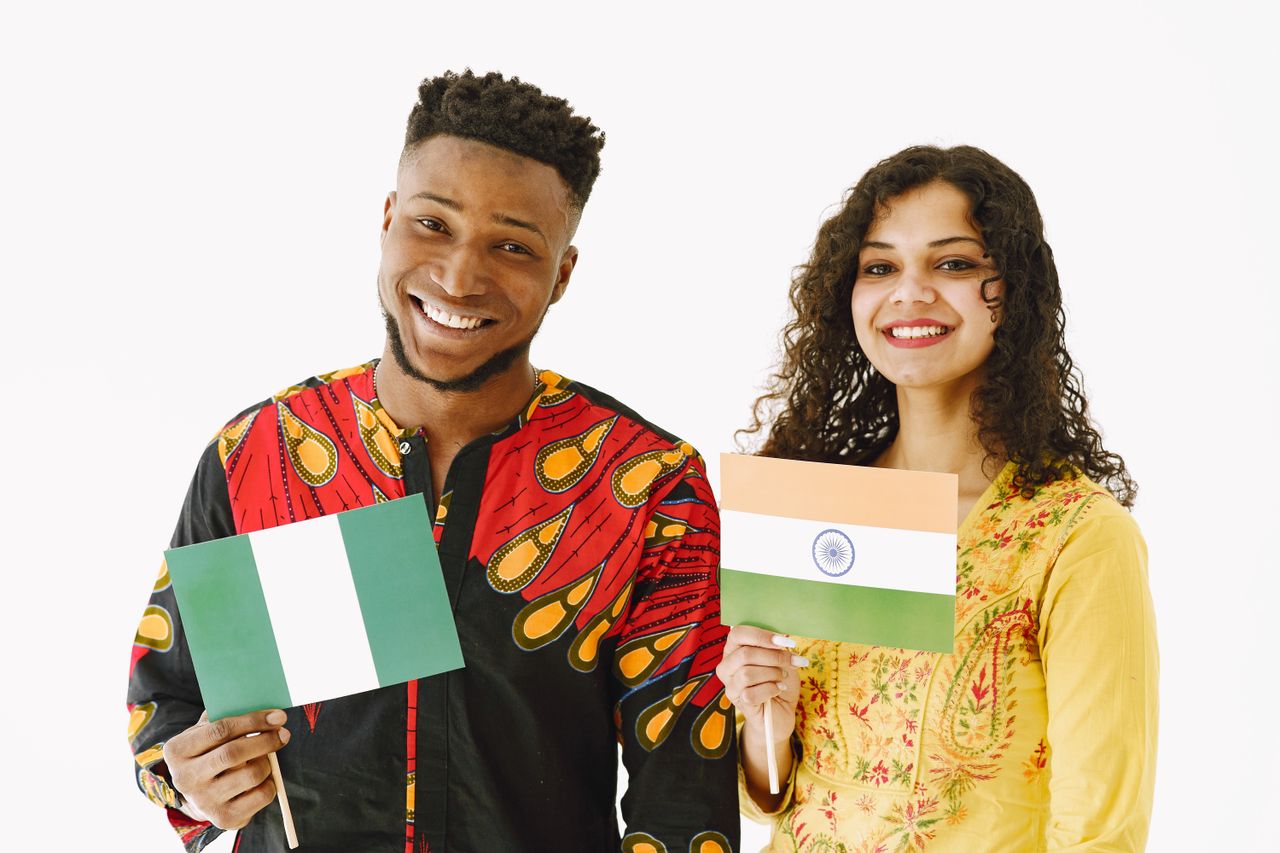 A Nigerian man and Indian woman smiling while holding their country's flags indoors.