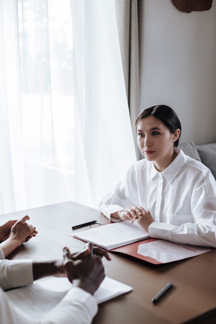 An Asian woman in a dress shirt attentively listens during a business meeting indoors.